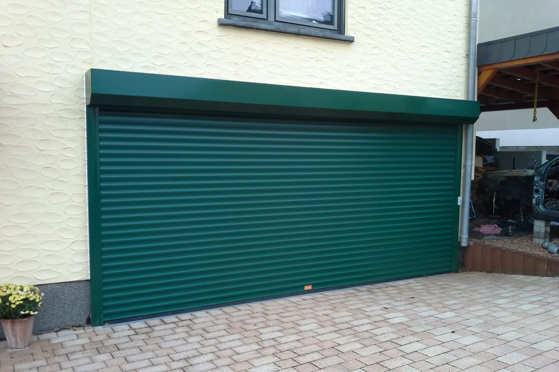 Grünes Rolltor an einer Garage mit strukturierter heller Außenfassade.