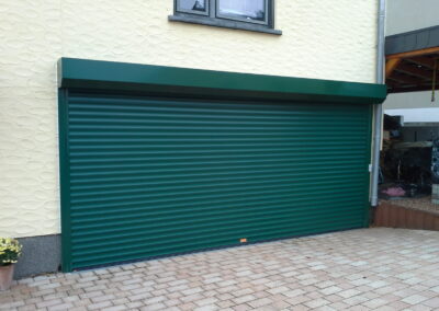 Grünes Rolltor an einer Garage mit strukturierter heller Außenfassade.