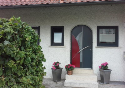 Graue Haustür mit rotem Gestaltungselement und Glasausschnitt