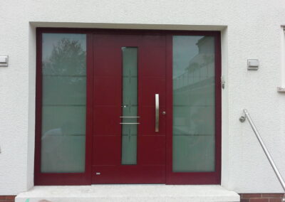 Rote Haustür mit Glaseinsatz und seitlichen Glaselementen