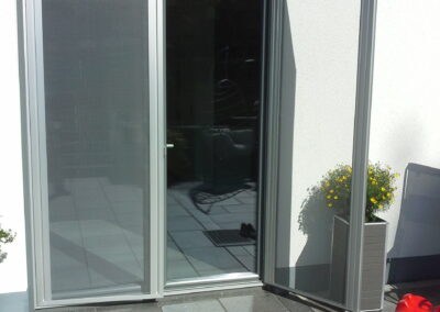 Geöffnete Terrassentür mit Fliegengitter vor einem Wohnhaus.